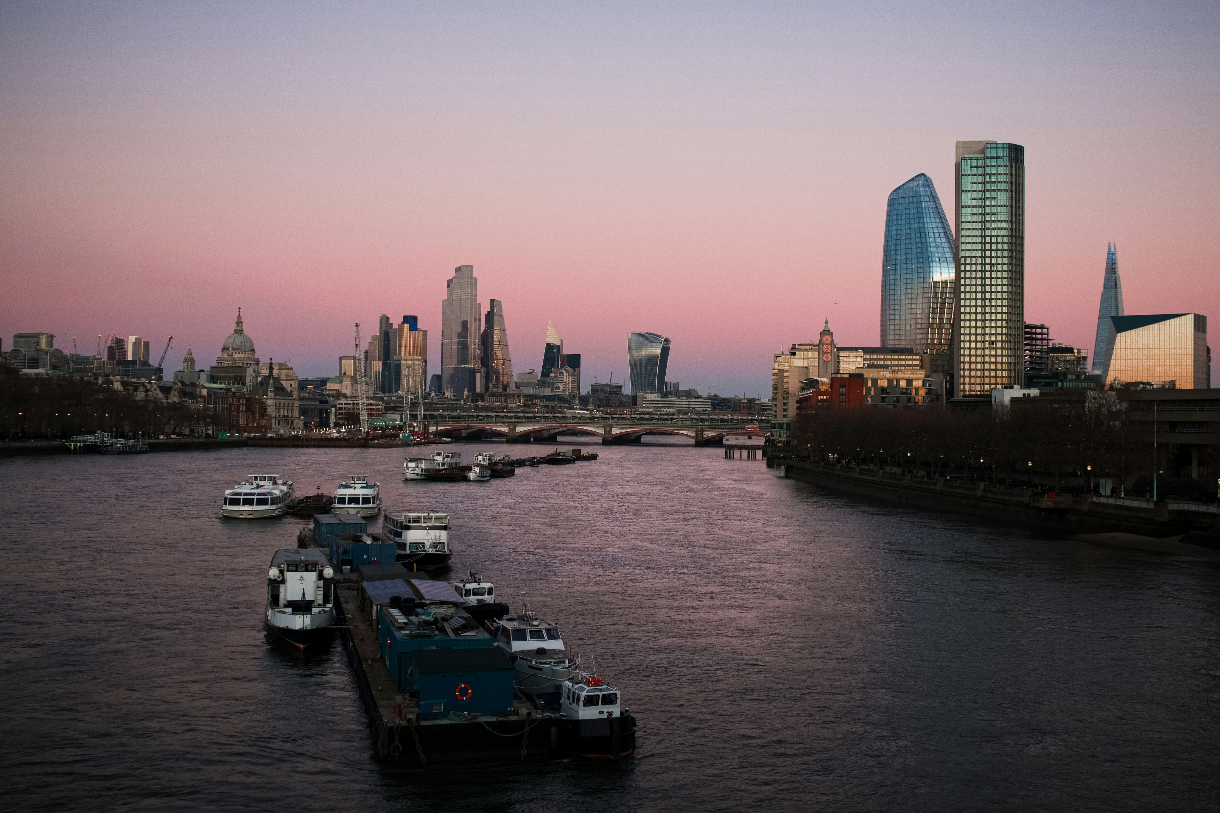 Boats travelling on the Thames with the London skyline in the background.