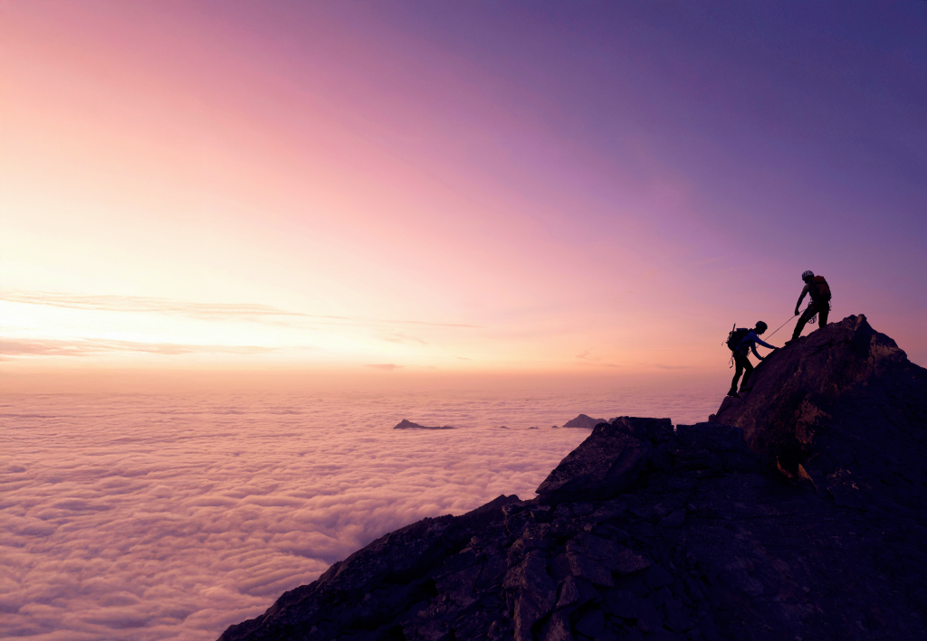Two hikers looking over a mountain landscape at sunrise.